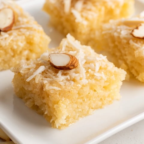Moist Egyptian Basbousa coconut cake, a golden dessert, is drizzled with sweet syrup, ready to serve.