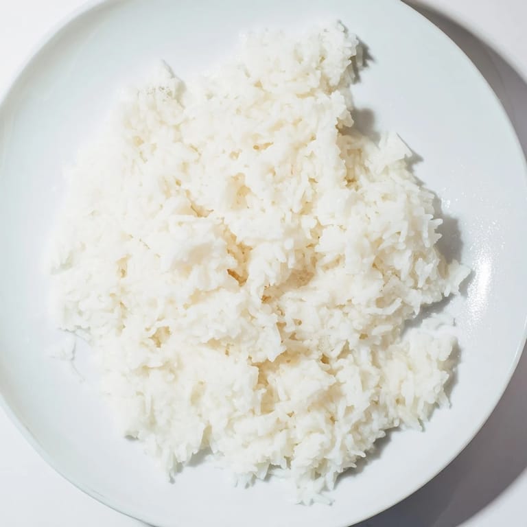 A steaming bowl of creamy Coconut Jasmine Rice, perfect as a side dish, with grains visible in the light.